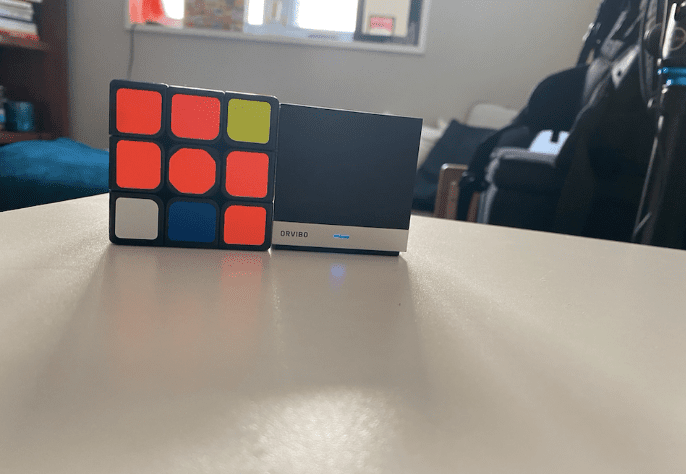 Orvibo's Magic Cube spočívající na stole vedle Rubikovy kostky pro srovnání velikostí
