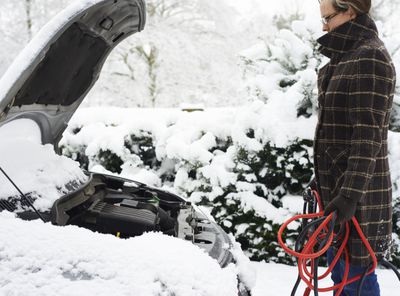 Muž, který držel startovací kabely ve sněhu před autem s kapucí nahoru