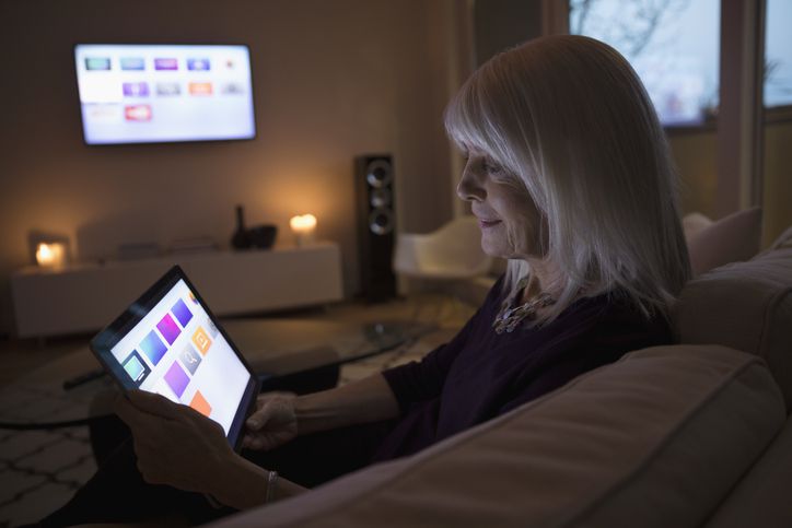 Osoba používající aplikace smart TV na digitálním tabletu na pohovce v obývacím pokoji