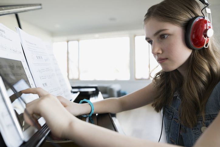 Zaměřená dívka s digitálním tabletu sluchátka na klavír