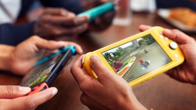 Tři lidé hrající Super Mario Kart 8 na Nintendo Switch a dvě konzole Nintendo Switch Lite.