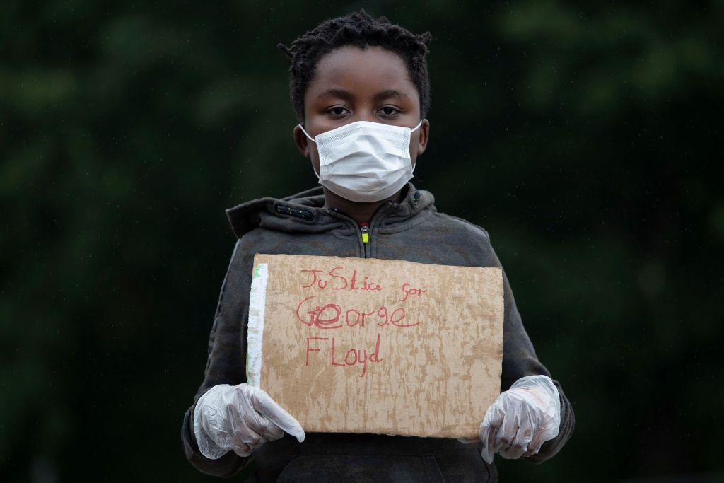 Maskovaný mladý člověk s protestním znamením George Floyd 