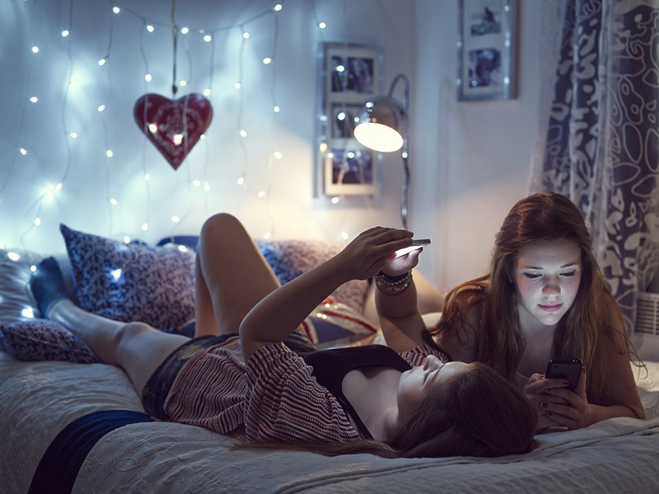 Dívky sedí v posteli a dívají se na telefony