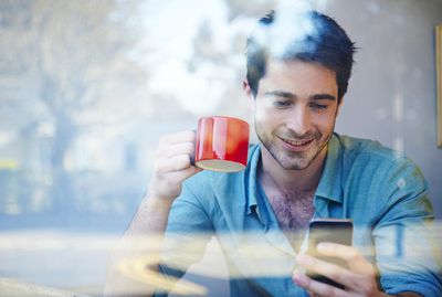 Člověk při pohledu na svůj telefon ve výloze kavárny