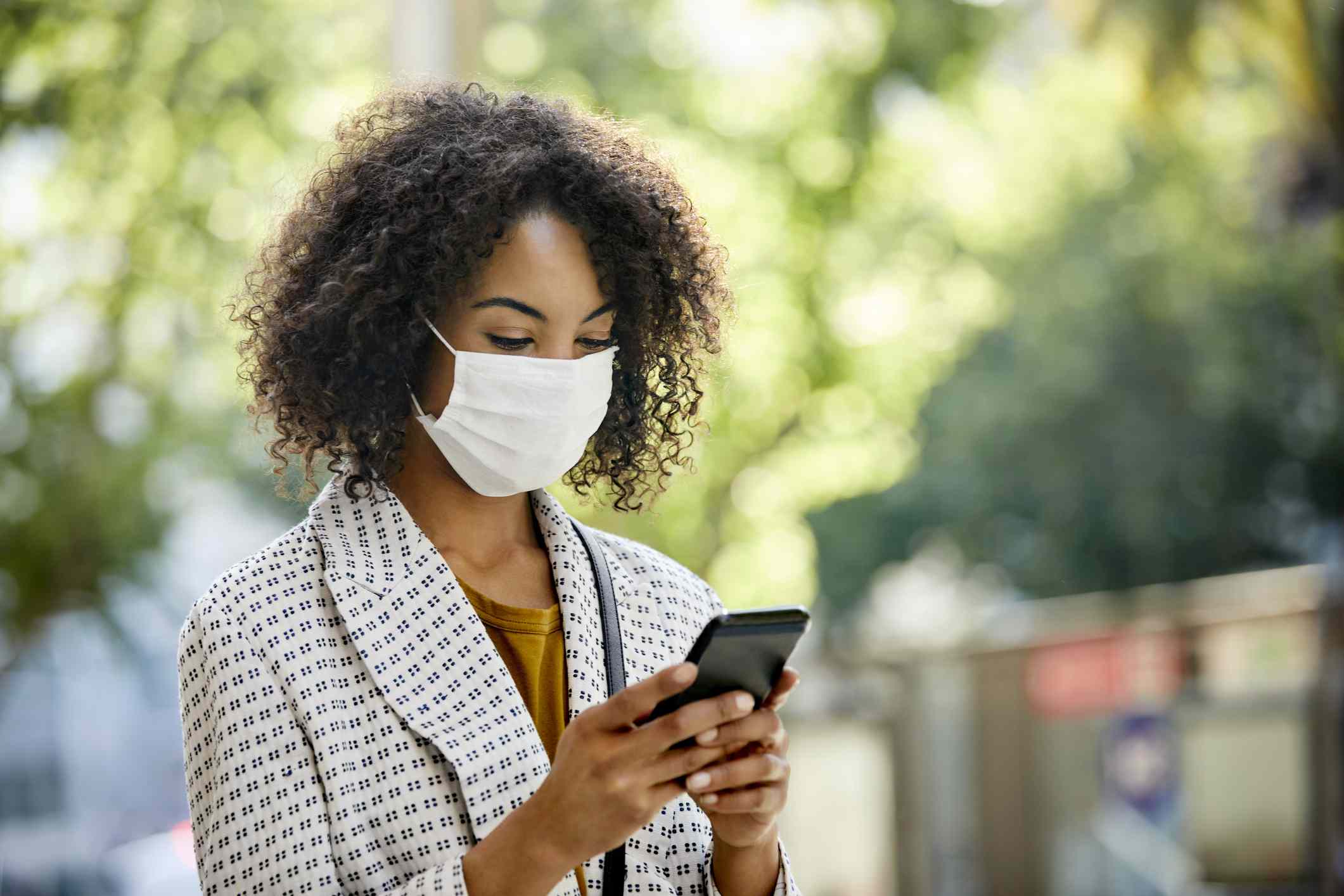 Žena nosí obličejovou masku, když stál venku a při pohledu na její smartphone