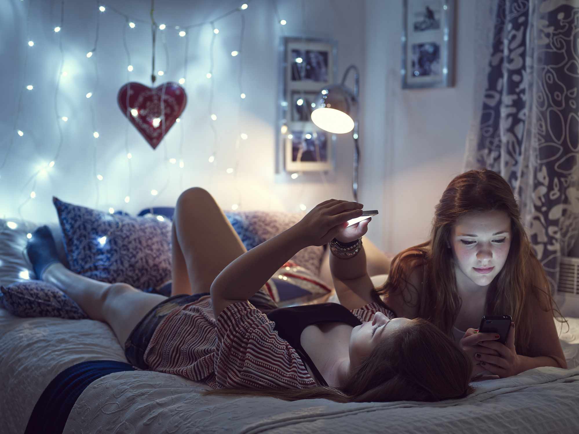 Dvě mladé ženy leží na posteli.  Světla na úpatí postele.
