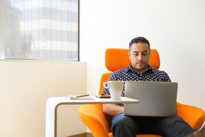 Muž pomocí přenosného počítače na oranžové židli