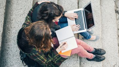 Dva studenti univerzity psaní poznámek na papírový notebook a notebook