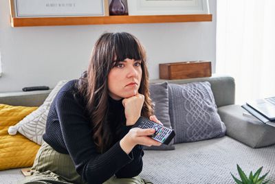 Žena, která se dívá znuděně na televizi mimo obrazovku, zatímco drží dálkové ovládání