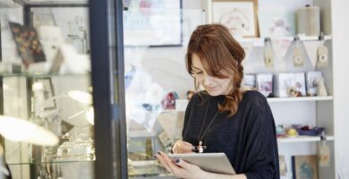 a mature woman using a digital tablet using the touch screen stock taking in a small gift shop 595914209 5a65a03147c2660037e3a69f