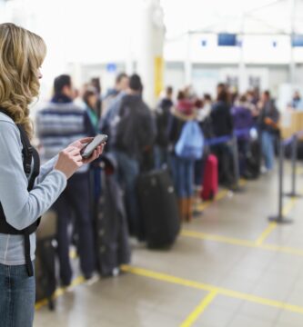 female traveller texting at airport check in desk 142309131 5a0b352813f1290037c17caf