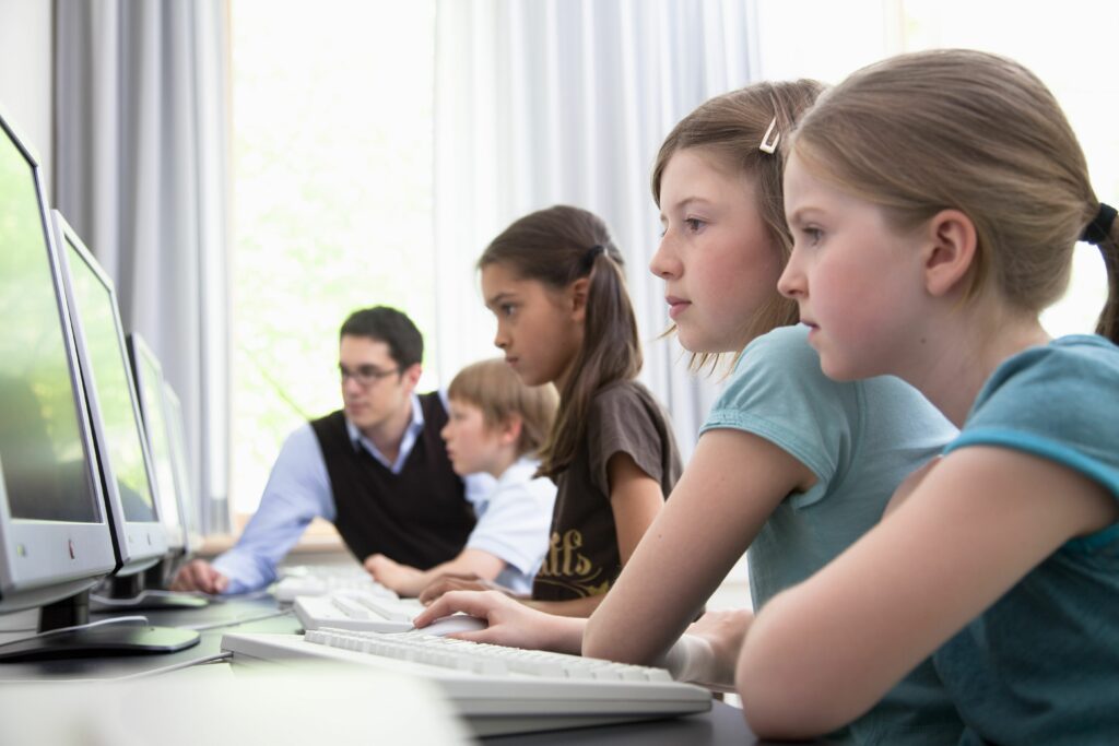 male teacher helping pupils in computer room hamburg germany 98188364 5880eb675f9b58bdb37465ed