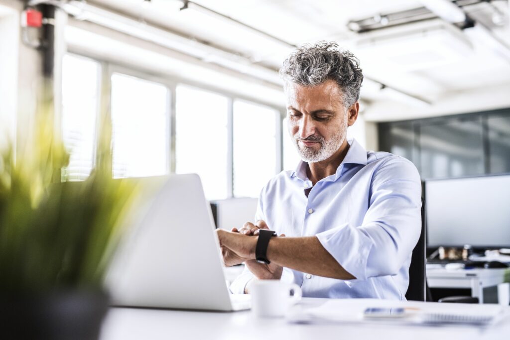 mature businessman sitting at desk in office looking at smartwatch 951529850 5b1abded8023b900366f9472