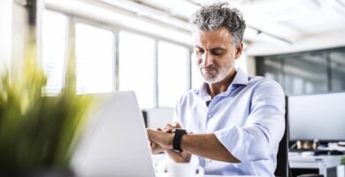 mature businessman sitting at desk in office looking at smartwatch 951529850 5b1abded8023b900366f9472