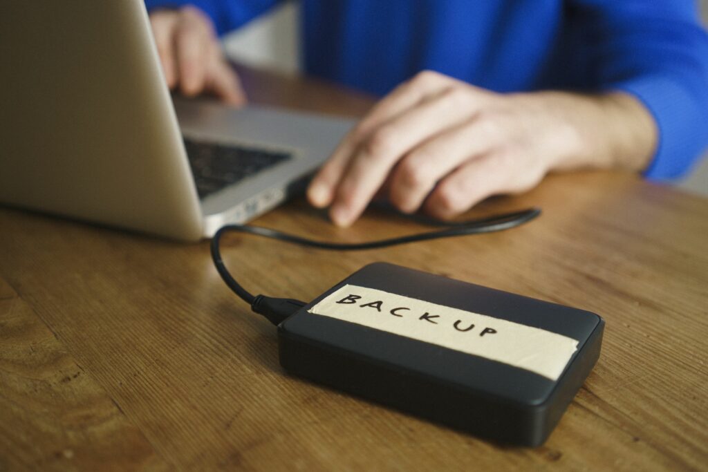 midsection of man using laptop with backup label on external hard disk drive at table 962574588 5b79f883c9e77c00572b2b8c