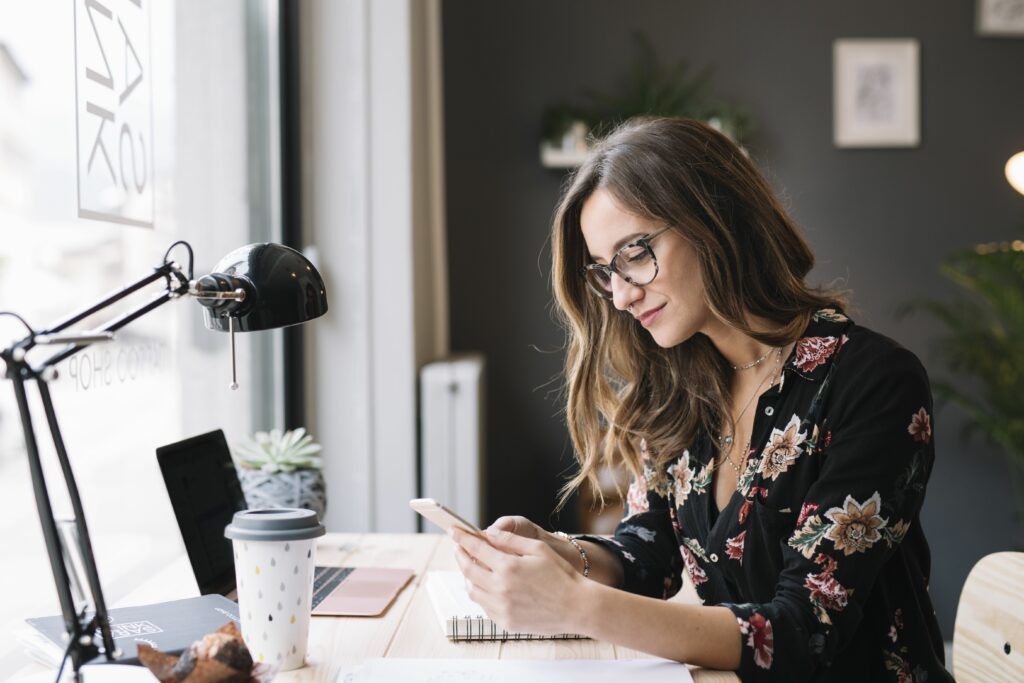 smiling woman sitting at desk in tattoo studio looking at cell phone 909590788 5c1abaadc9e77c0001f4ae5f