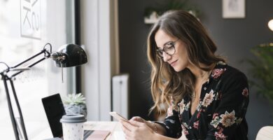 smiling woman sitting at desk in tattoo studio looking at cell phone 909590788 5c1abaadc9e77c0001f4ae5f