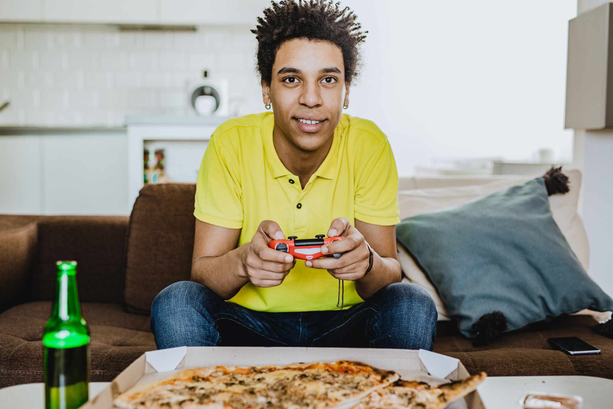 Mladý dospělý hrající videohry nad pizzou a drinkem.
