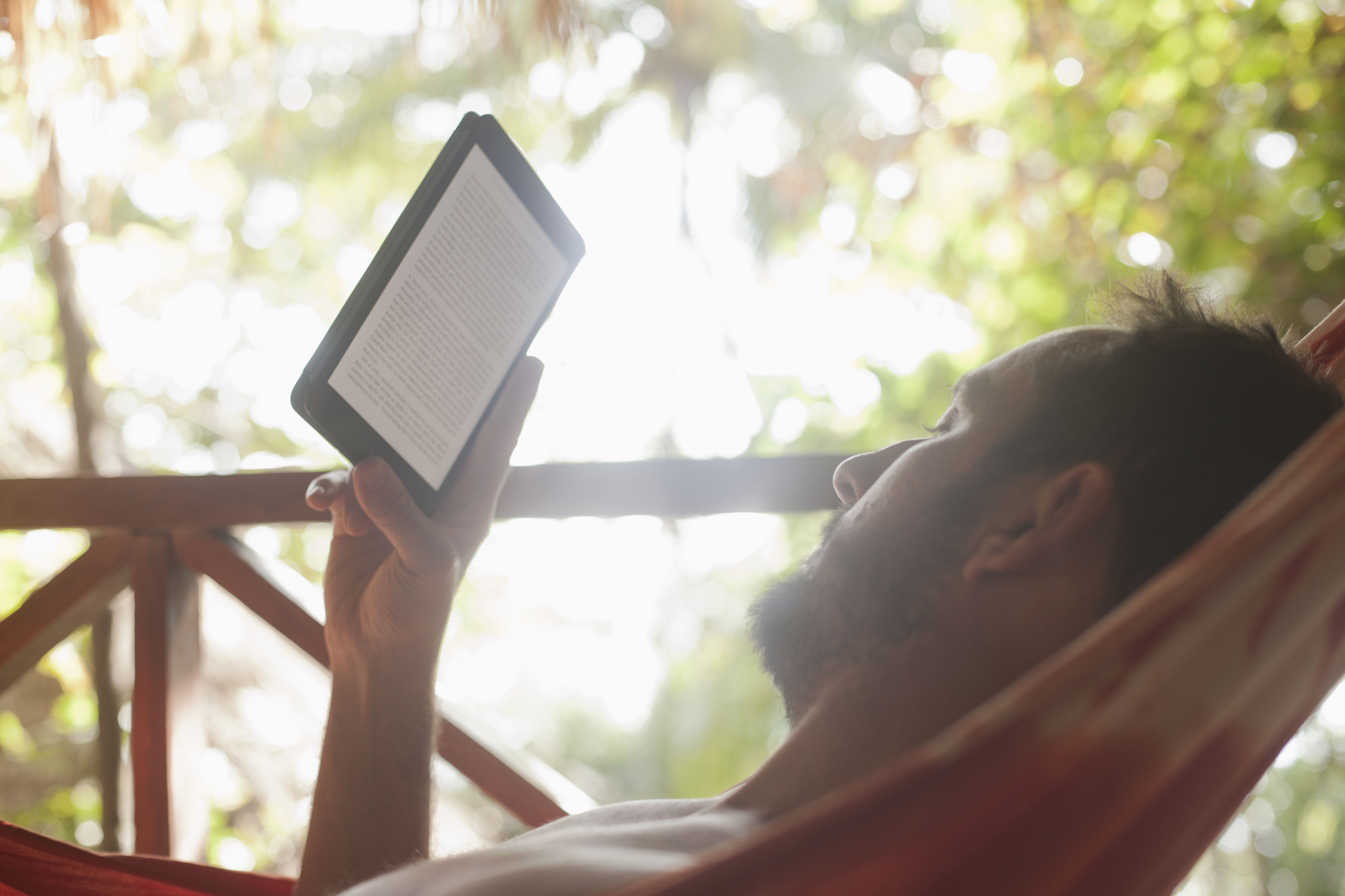 Muž relaxační v houpací síti čtení z digitální knihy