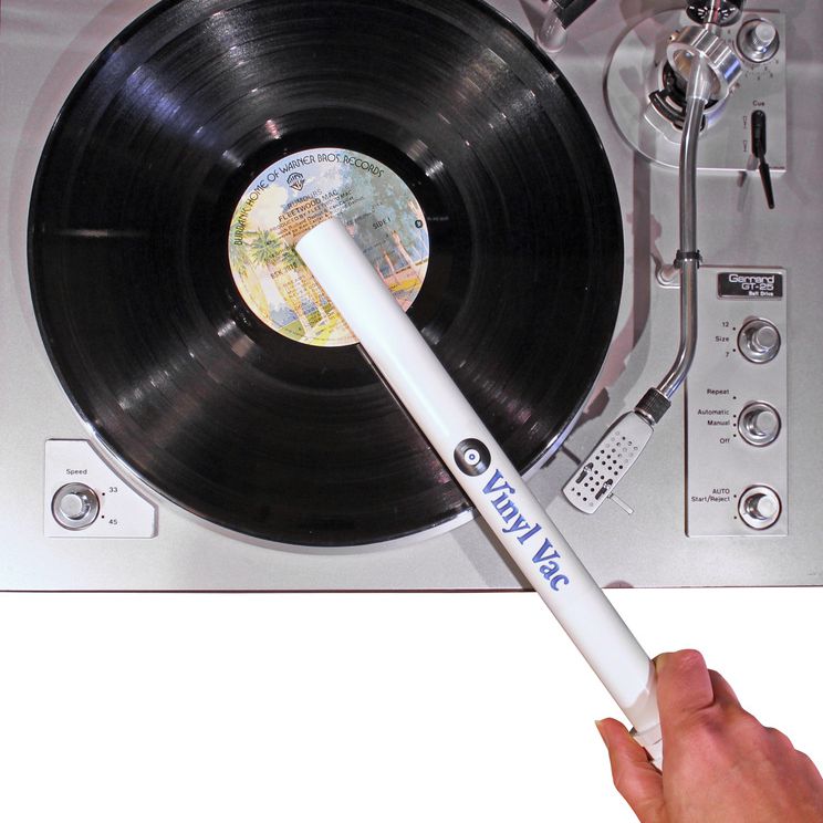 Ruka držící vinylový vysavač k čištění desky ležící na gramofonu
