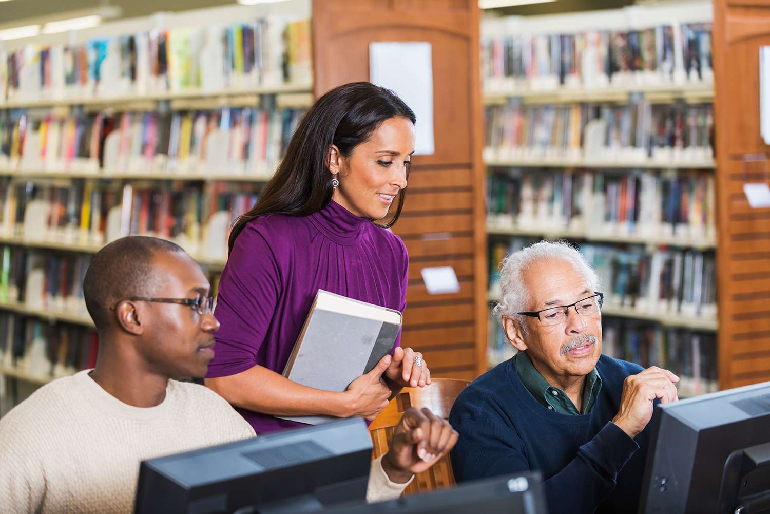 Lidé pomáhají starší muž používat počítač v knihovně