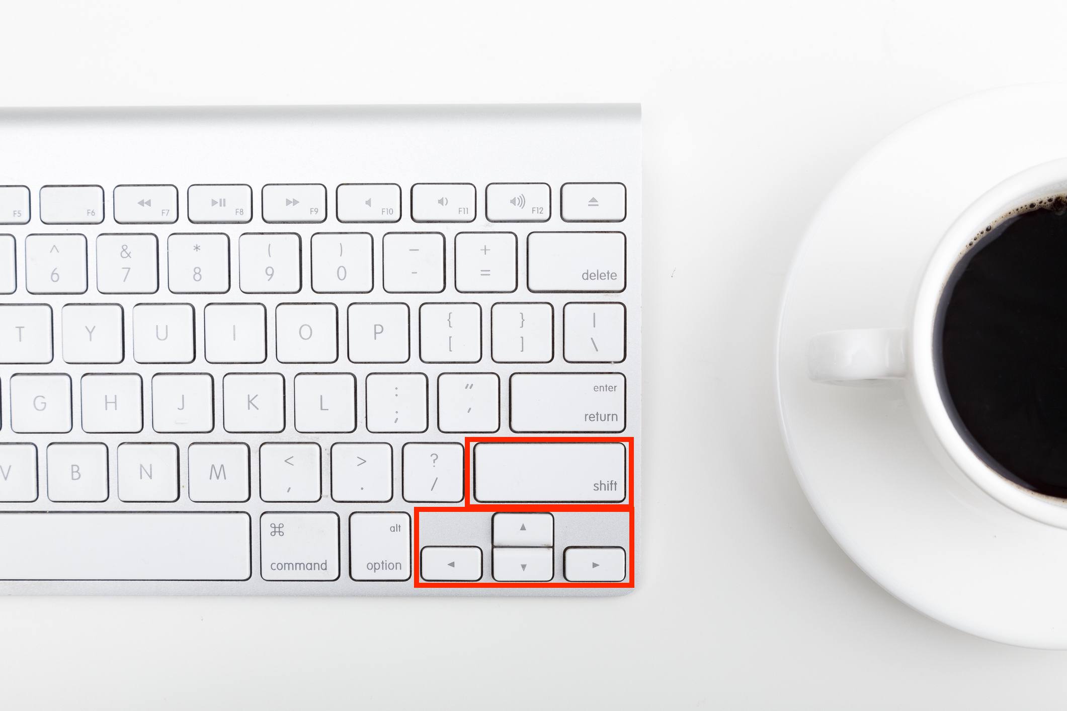 Přímo nad záběrem šálku kávy a počítačové klávesnice na stole označujícím klávesy Shift a Šipky