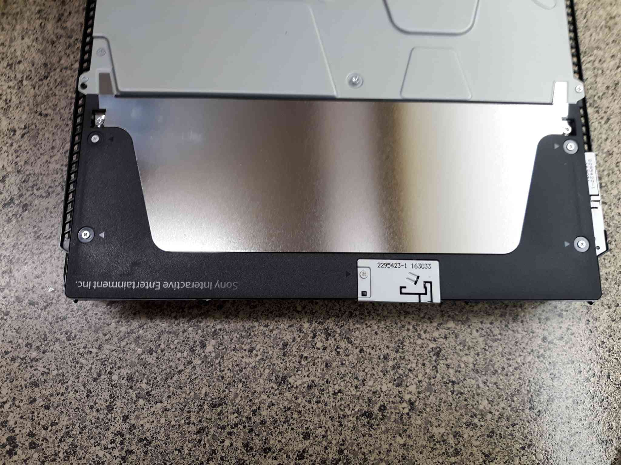 Pomocí křížového šroubováku odstraňte černý plastový kryt poblíž zadního konce konzoly PS4.
