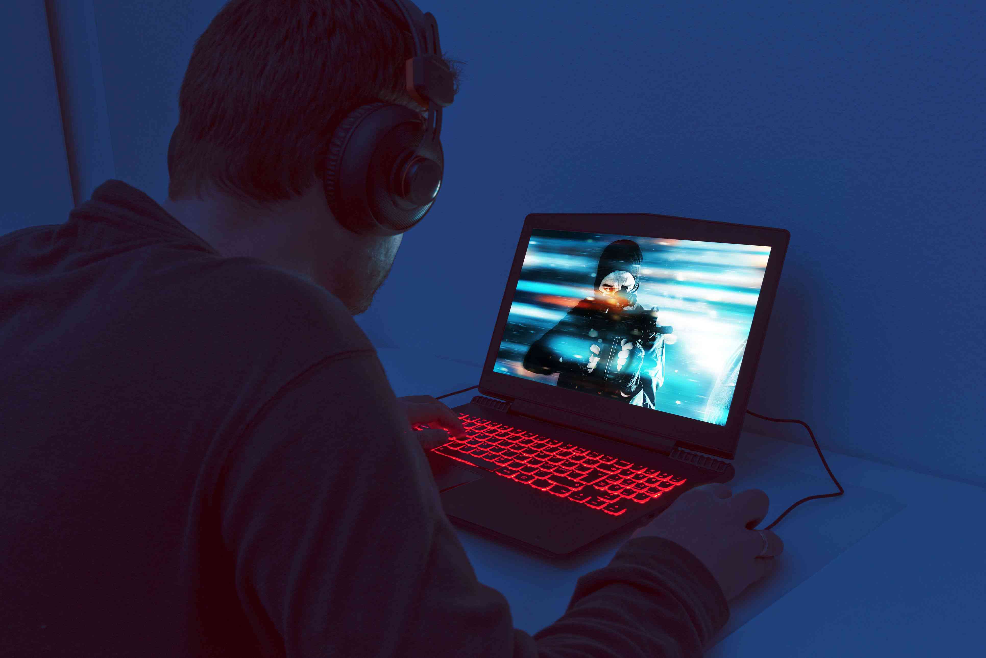Muž sedí sám před herním notebookem a hraje videohru