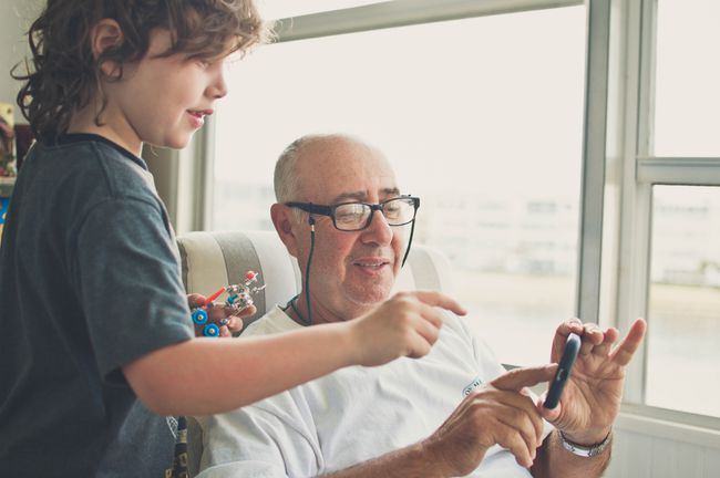 Prarodič a vnouče komunikují s chytrým telefonem, zatímco dítě drží malého robota.