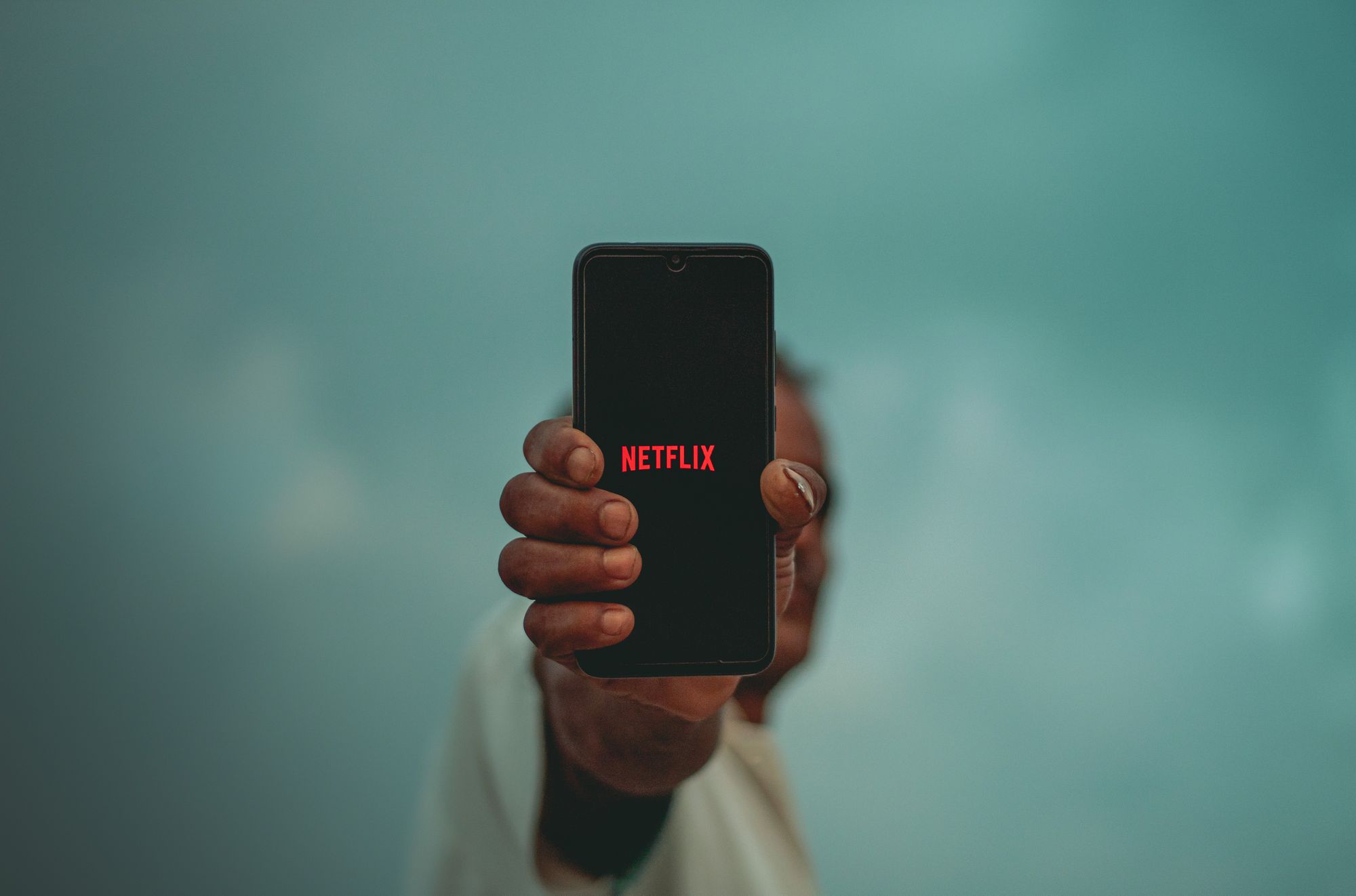 Osoba držící černý iPhone na délku paže s logem Netflix na obrazovce. 