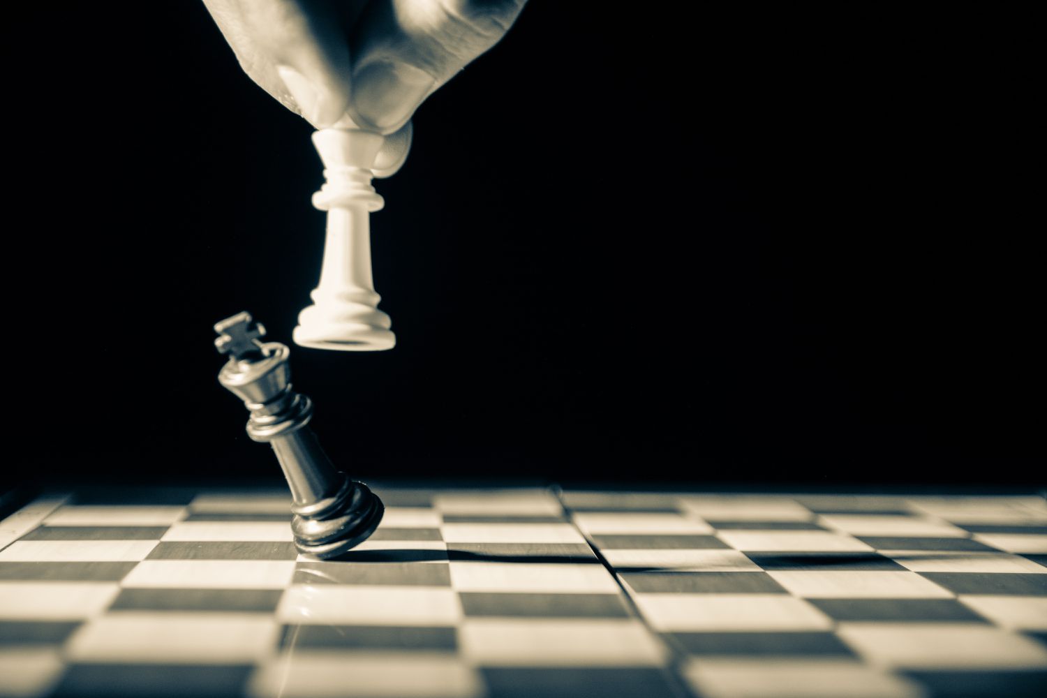 Detailní obrázek ve stupních šedi bílého šachového krále, jak sundává černého šachového krále. 