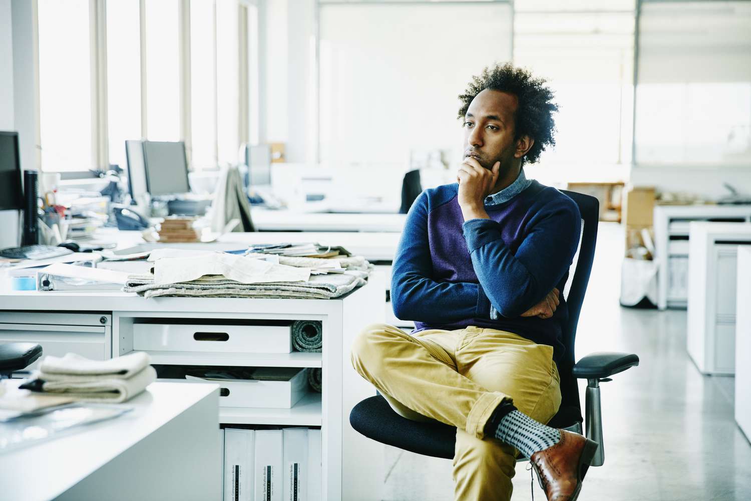 muž s rukou na bradě sedící na pracovní stanici v kanceláři