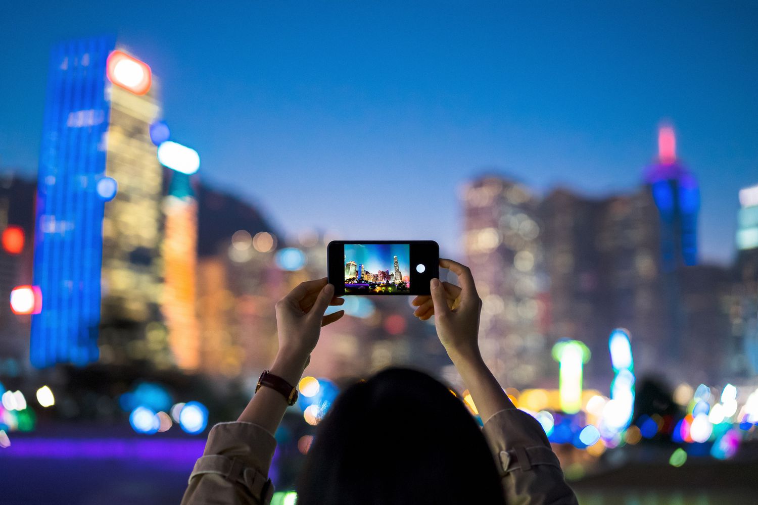 Někdo pomocí chytrého telefonu vyfotografuje panorama města za soumraku.